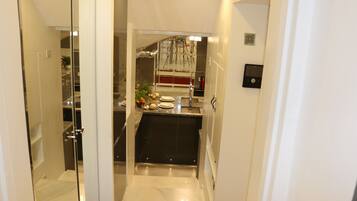 A narrow hallway leading to a kitchen with a marble countertop, a sink, and a stainless steel range hood.