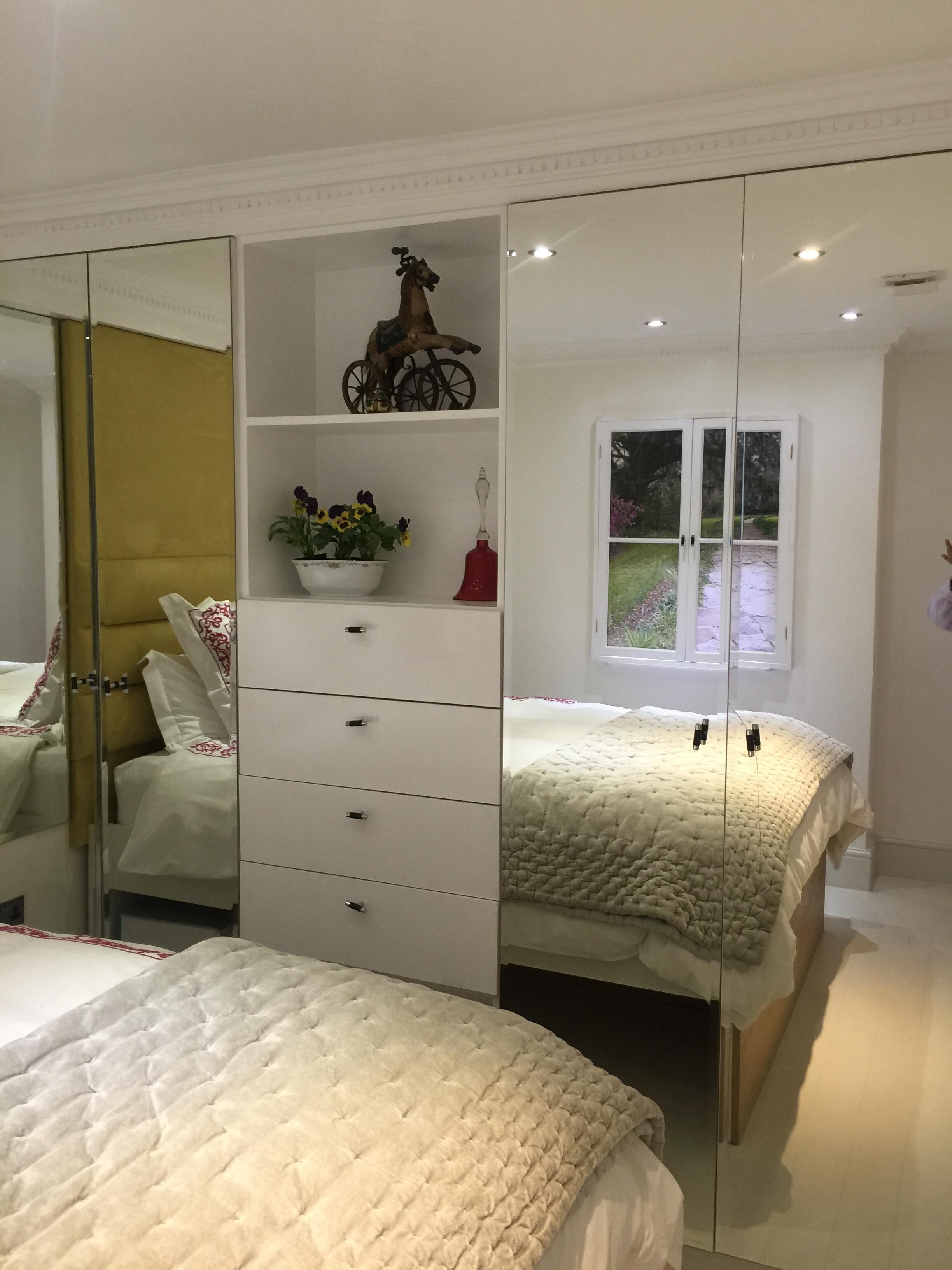 Un dormitorio con un espejo grande, una cama con edredón acolchado, un aparador con cajones, una planta en maceta y una bicicleta decorativa en la estantería.