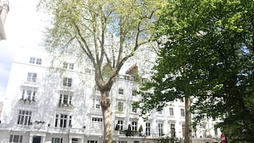 A white building with multiple windows and balconies, surrounded by trees.