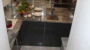 Een keuken met granieten aanrecht, een RVS spoelbak en een zwarte spatwand.