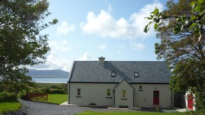 A house with a grey roof, a red door, and a view of the sea and mountains in the background. - Traditional style cottage free WiFi short walk from Reenroe Beach Ballinskelligs (Ballinskelligs)