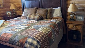 Un dormitorio acogedor tipo cabaña de madera con una cama grande, un cabecero de madera y una imagen enmarcada de un ciervo en la pared.