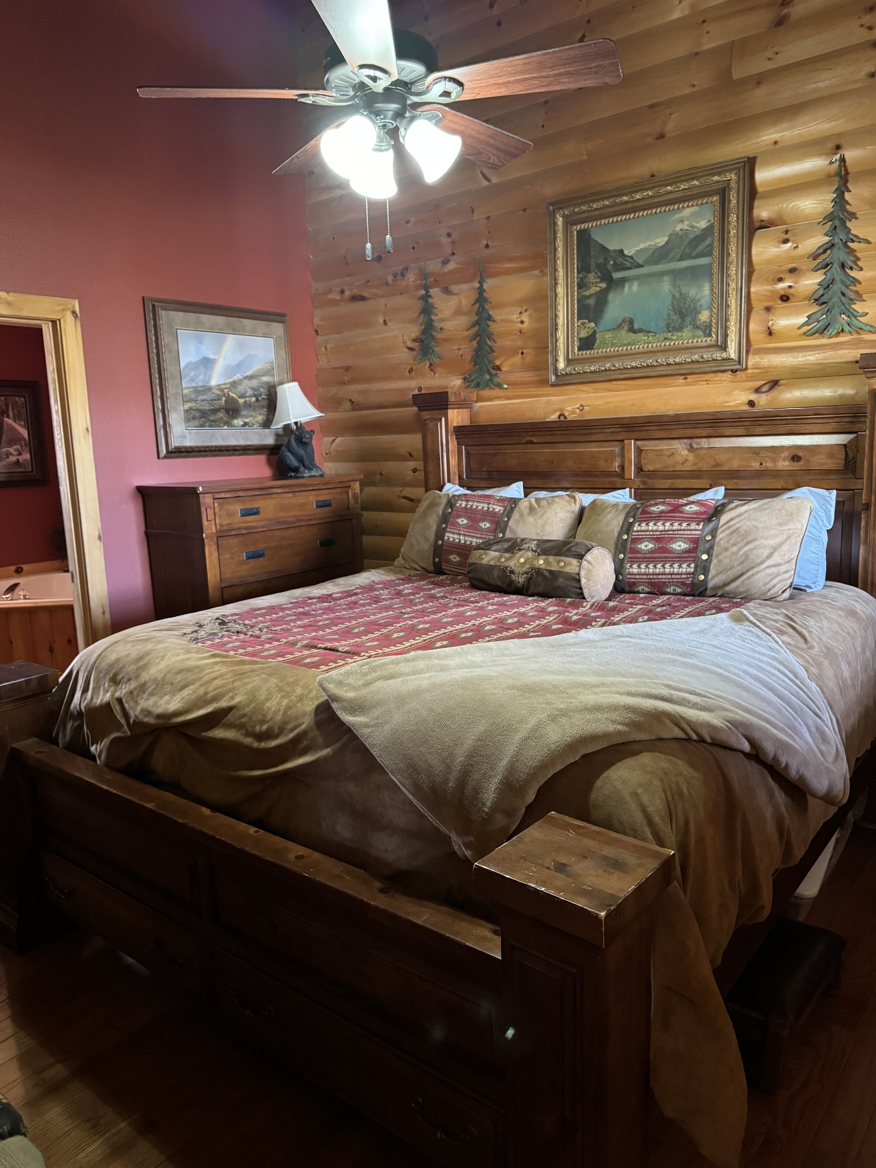 A wooden bedroom with a bed, a ceiling fan, and a framed landscape painting.