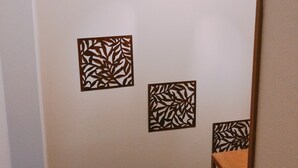 A hallway with a light fixture, a wooden trim, and three wall-mounted decorative panels. - Ryokoheya Hankyukan (Osaka)