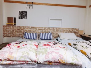 A bed with floral bedding, a brick headboard, and a wall-mounted light fixture. - Ryokoheya Hankyukan (Osaka)