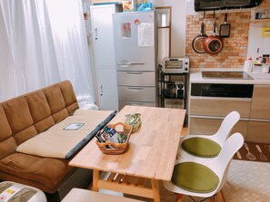 A compact kitchen with a refrigerator, toaster, and stove. There's a dining area with a brown sofa and a small table. - Ryokoheya Hankyukan (Osaka)