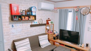 A living room with a sofa, TV, and shelves with various items. - Ryokoheya Hankyukan (Osaka)