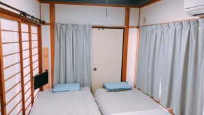 A room with two beds, wooden paneling, a ceiling fan, and a sliding door. - Ryokoheya Hankyukan (Osaka)