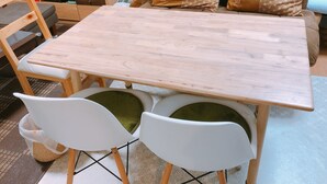 A wooden dining table with two white chairs, a television, and patterned cushions on a couch. - Ryokoheya Hankyukan (Osaka)