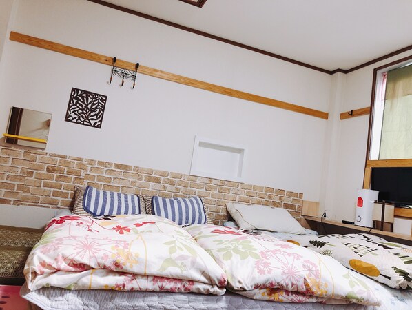A bedroom with a brick accent wall, a bed with floral bedding, a bedside table with a lamp, and a window with curtains.
