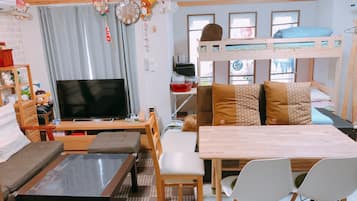 A cozy living room with a TV, sofa, bunk bed, and a dining table with chairs.