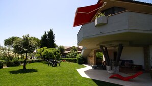 A modern house with a flat roof, a red awning, and a well-maintained lawn.