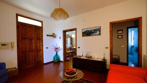 A living room with a glass coffee table, a red sofa, wooden doors, and a dining area in the background.