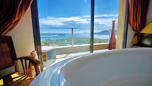 Habitación de hotel con una cama grande, vista al mar y un balcón con barandilla.