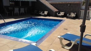 A rectangular swimming pool with a tiled edge, surrounded by lounge chairs and a tiled deck.