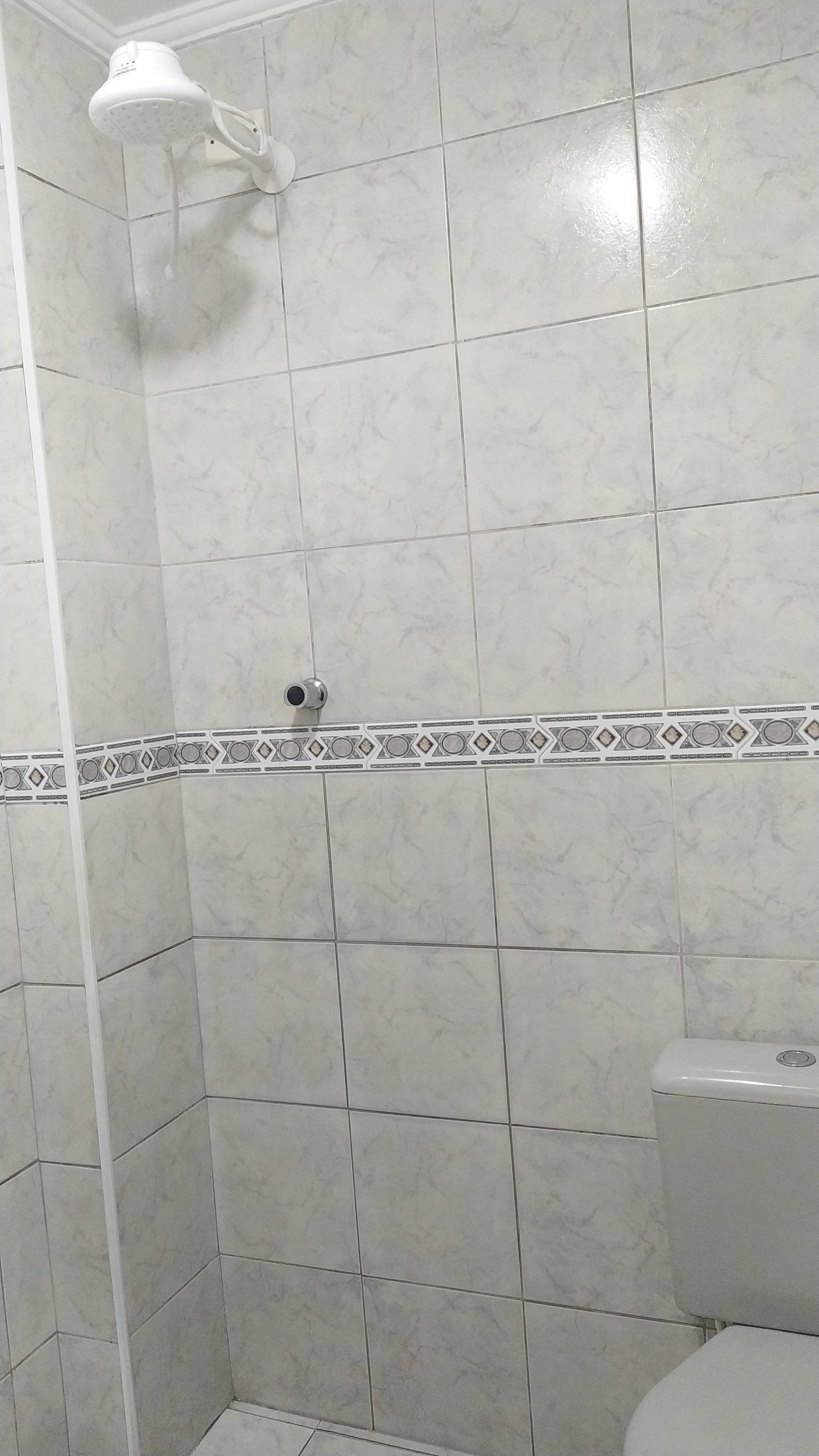 A bathroom with white marble tiles, a showerhead, and a toilet.