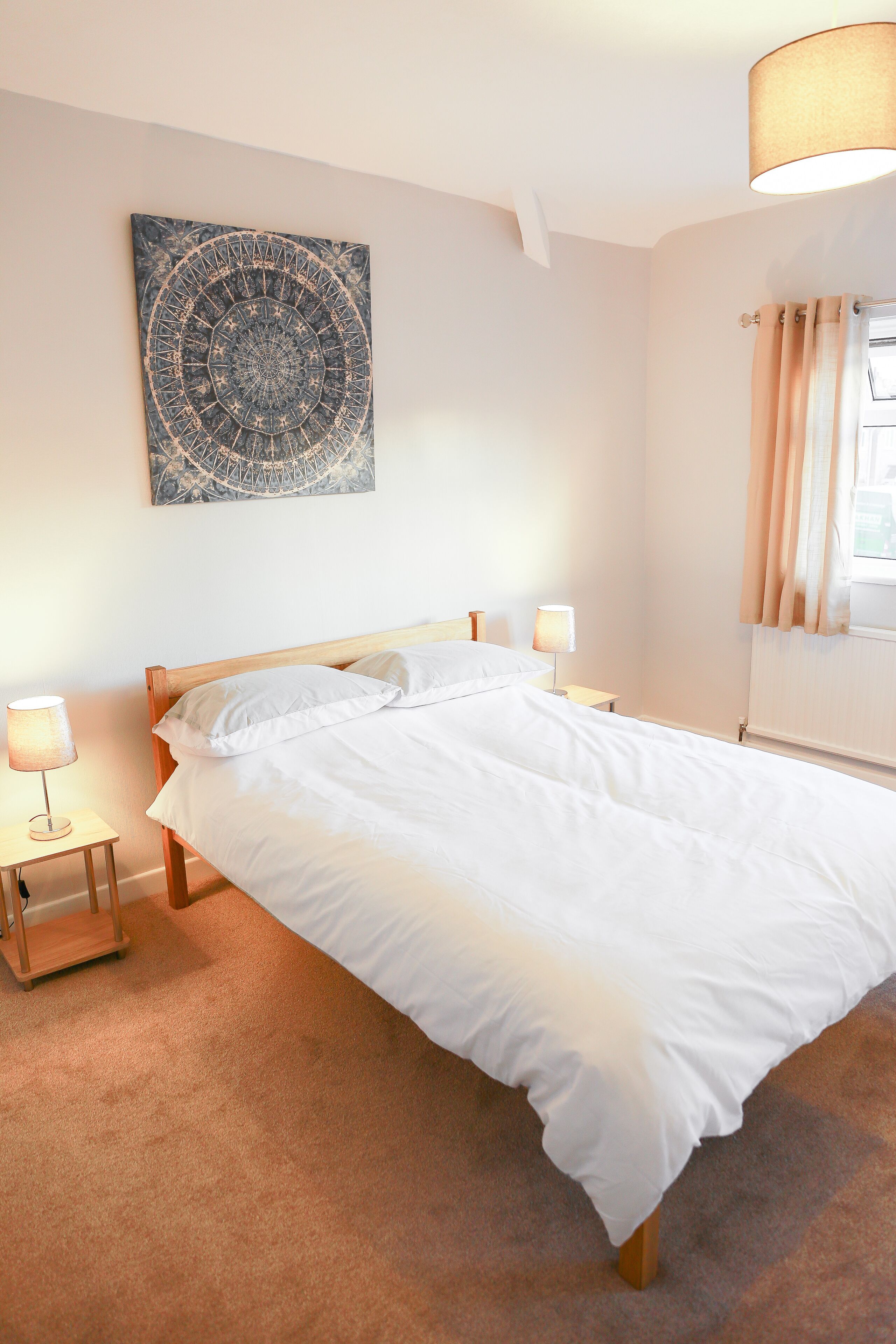 A neatly made bed with white linens, a wooden headboard, and two bedside lamps.