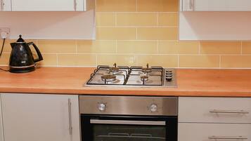 Una cocina con gabinetes blancos, cocina a gas, horno y cafetera.