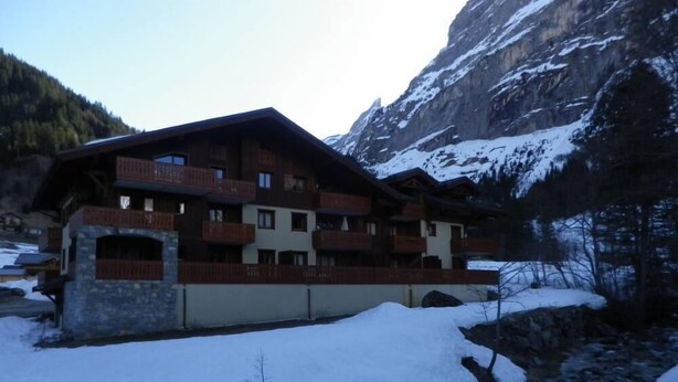 A multi-story chalet with balconies, set against a mountainous backdrop.
