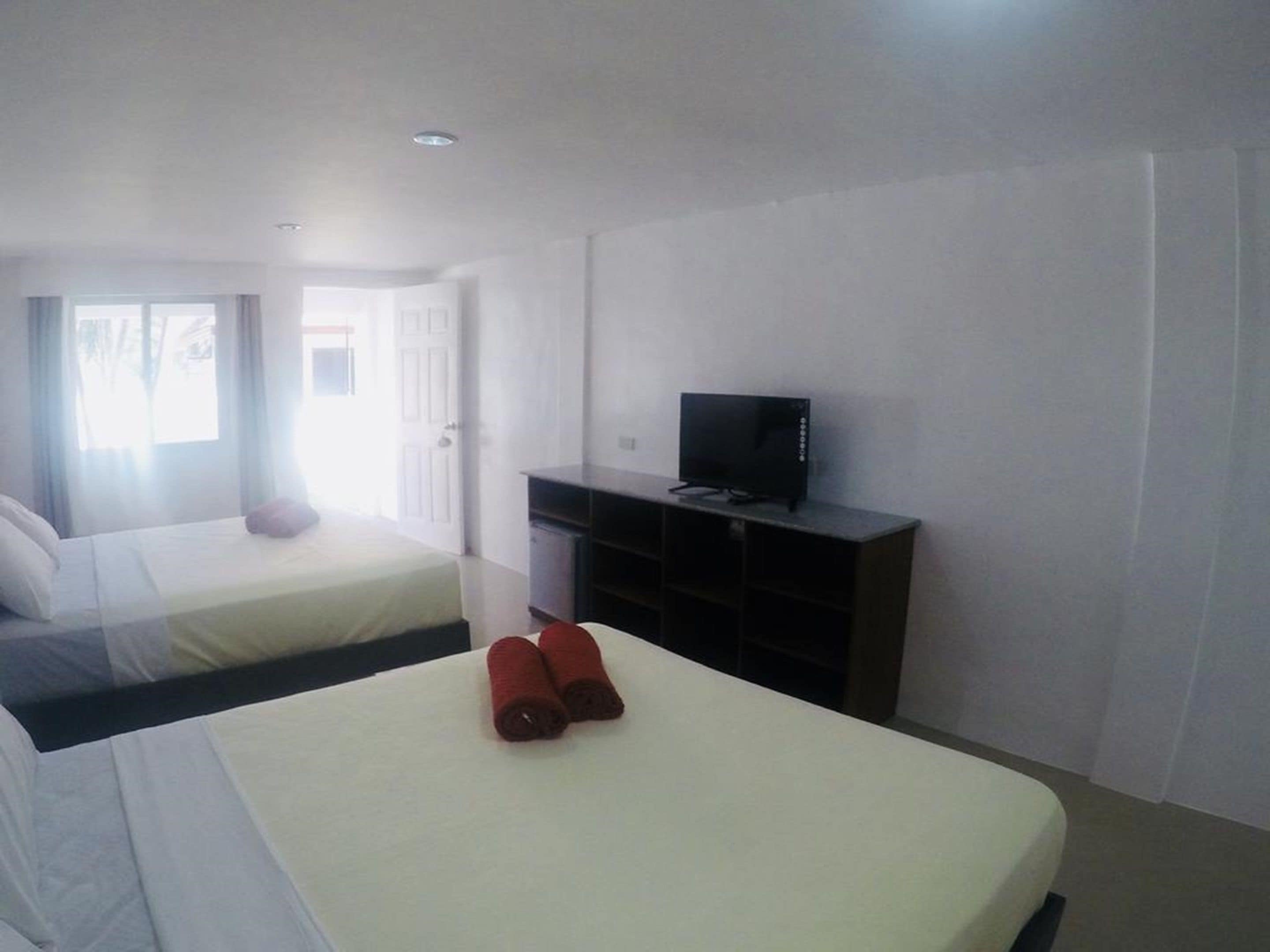 A hotel room with two beds, a TV on a stand, and a window with curtains.