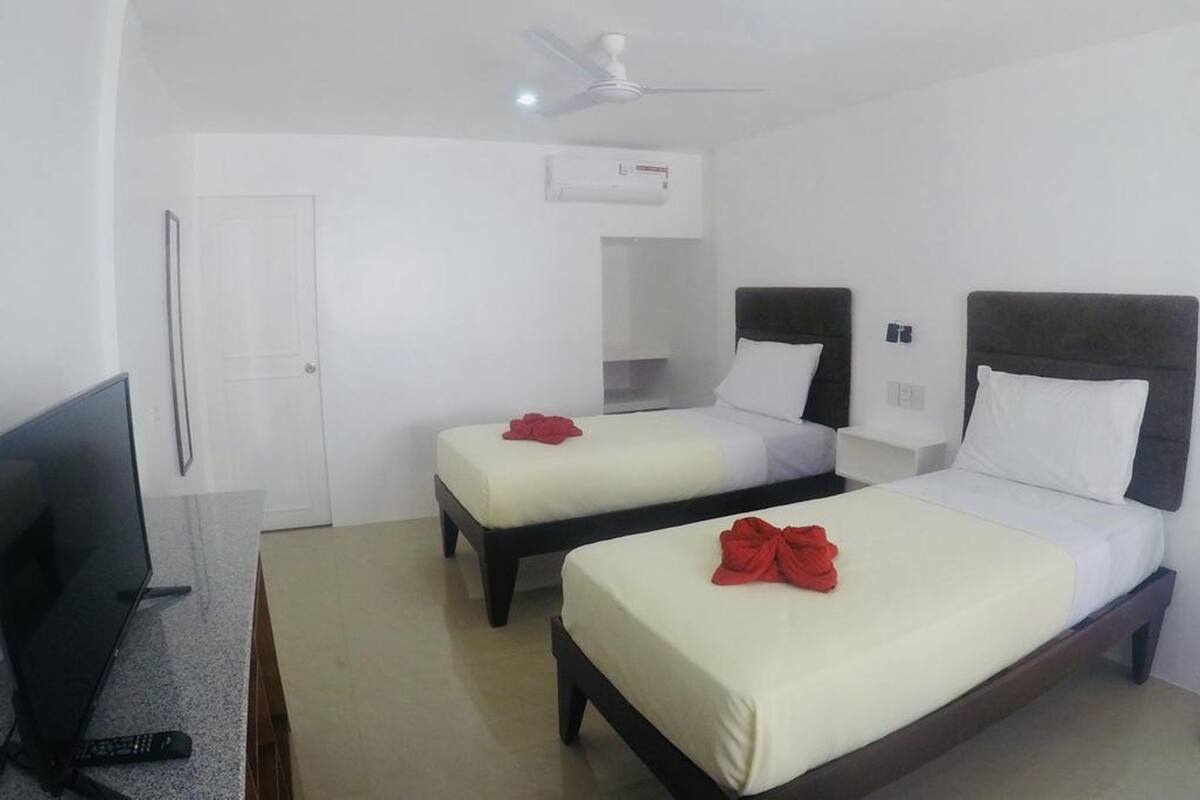 Habitación de hotel con dos camas, televisión y ventilador de techo.
