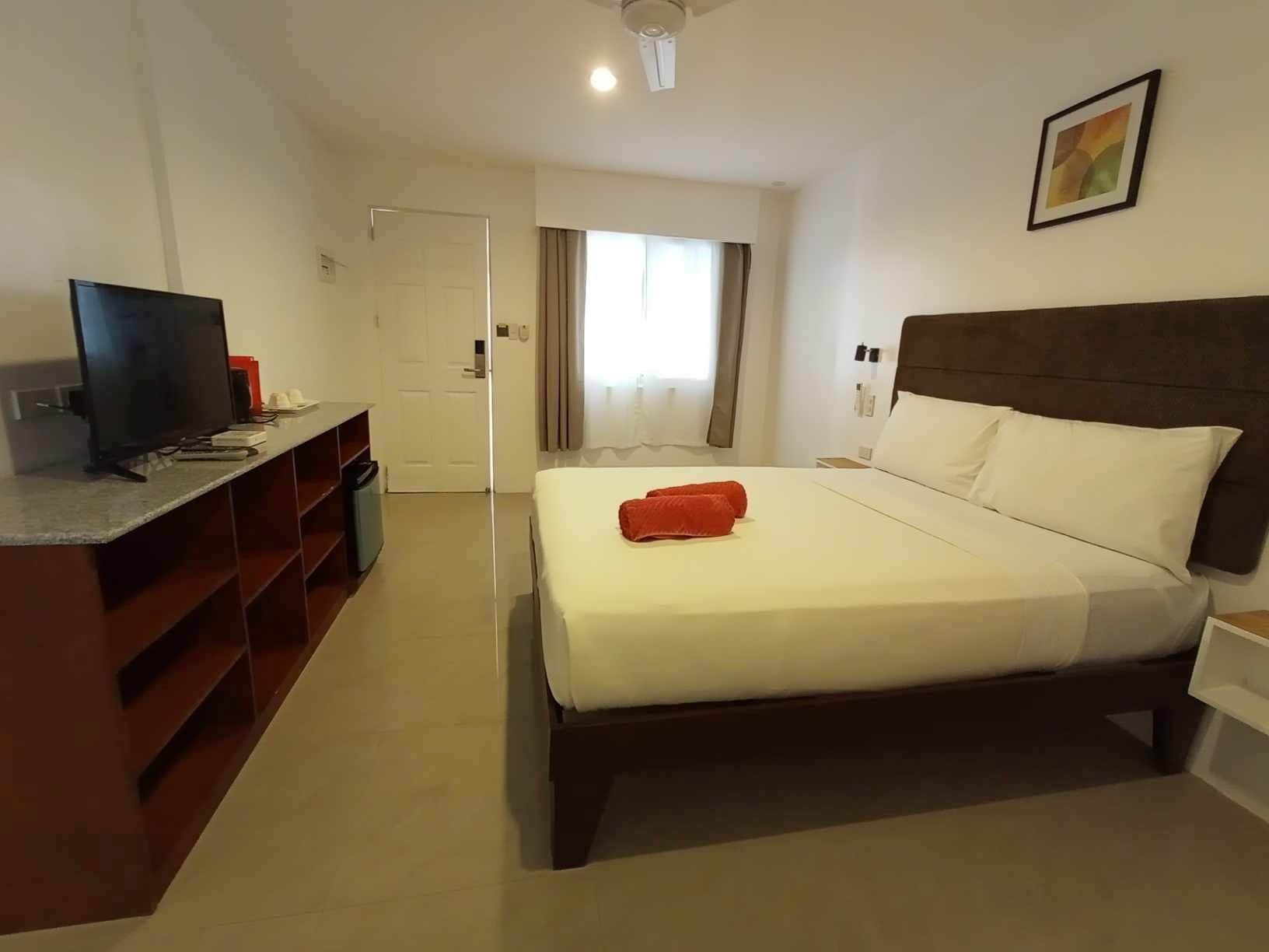 A hotel room with a bed, a desk, a television, and a window with curtains.