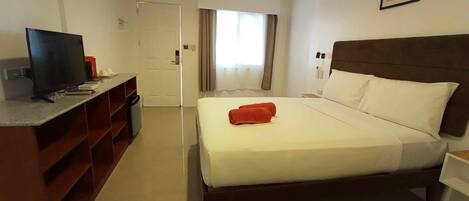 A hotel room with a bed, a desk, a television, and a window with curtains.