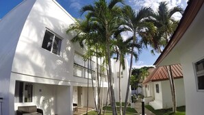 A modern white building with a balcony, palm trees, and a small outdoor seating area. - Heartland Hotel Service Rooms and Apartments (Panglao)