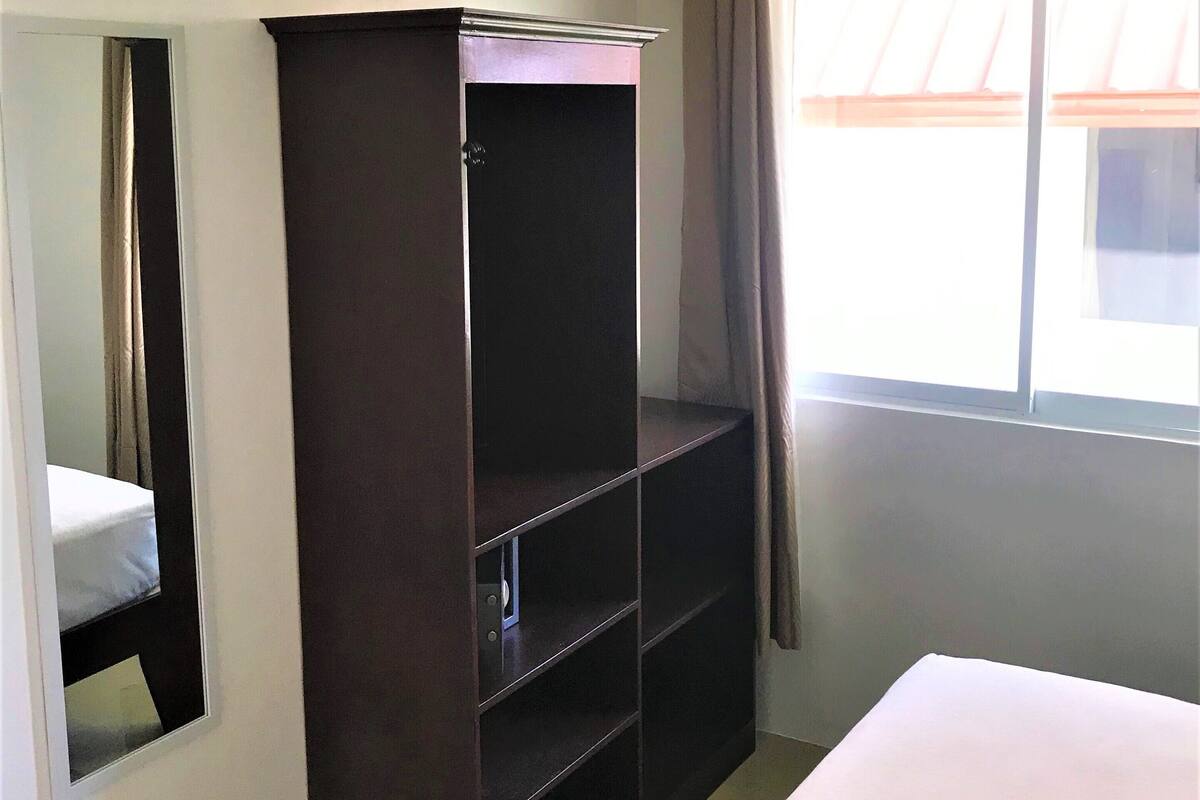 Una habitación de hotel con cama, armario, espejo y ventana con cortinas.