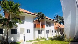 A modern hotel with a white facade and red roof, featuring a central courtyard with palm trees and a checkered pathway. - Heartland Hotel Service Rooms and Apartments (Panglao)