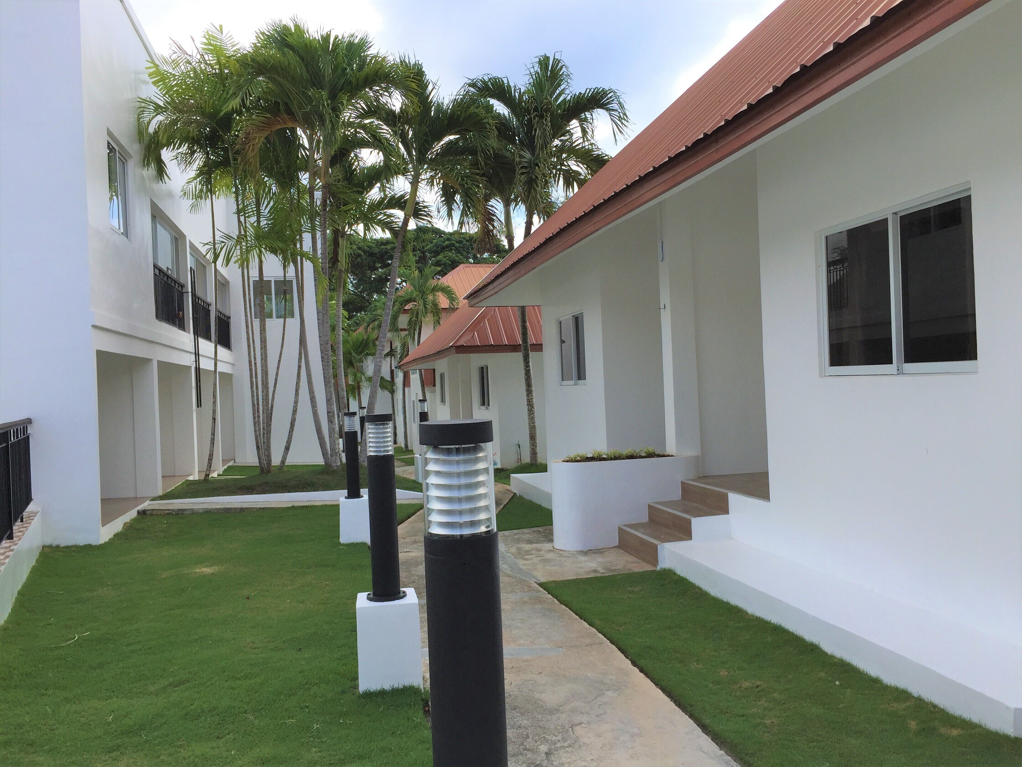A modern building with a red roof, white walls, and a narrow pathway flanked by palm trees.