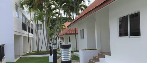 A modern building with a red roof, white walls, and a narrow pathway flanked by palm trees.