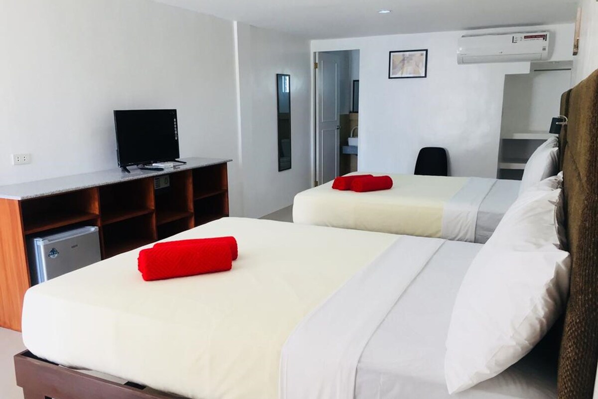 Une chambre d’hôtel avec deux lits, un bureau avec une télévision et une kitchenette.