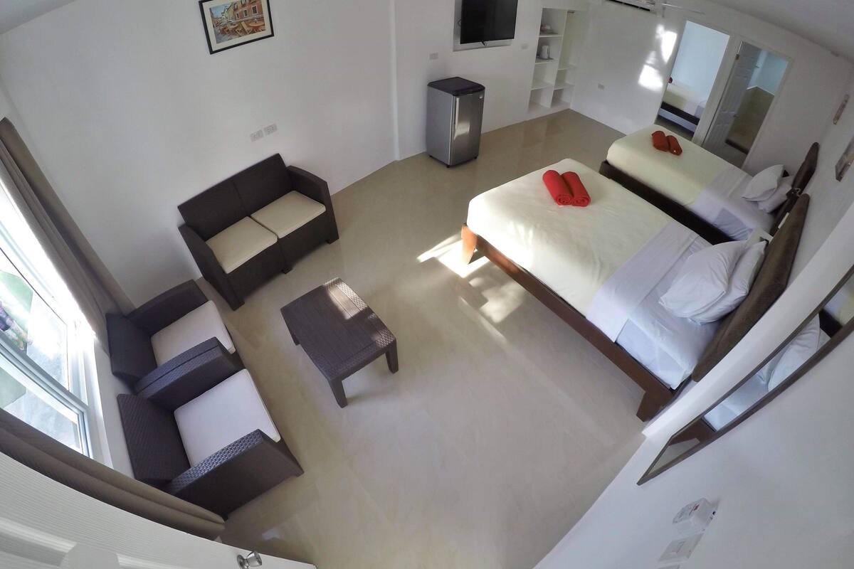 Una habitación de hotel con cama, sofá, una mesita, televisor y refrigerador.
