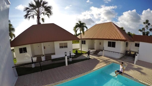 A swimming pool with a tiled deck, surrounded by buildings with red roofs and white walls. - Heartland Hotel Service and Apartments (Panglao)