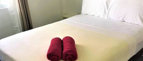 Un lit bien fait, avec des draps blancs et deux serviettes rouges enroulées, posées au pied du lit.