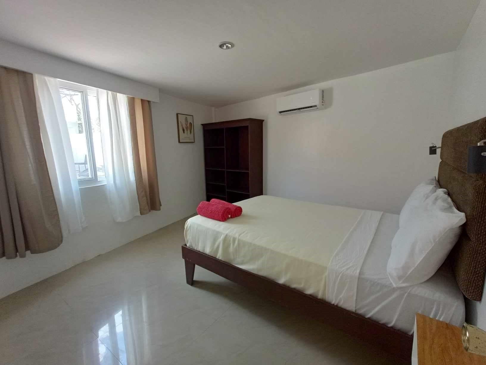 Un dormitorio con cama, armario, equipo de aire acondicionado y ventana con cortinas.