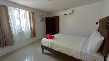 Un dormitorio con cama, armario, equipo de aire acondicionado y ventana con cortinas.