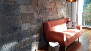 Una habitación con pared de piedra, piso de madera, sofá rojo y lámpara negra.