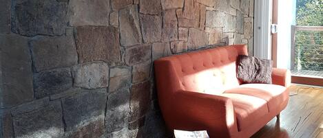 A room with a stone wall, a wooden floor, a red sofa, and a black lamp.