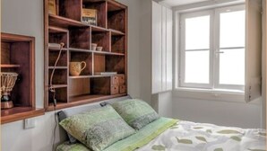 Une chambre à coucher avec un lit, une étagère en bois, une fenêtre et un petit tabouret.