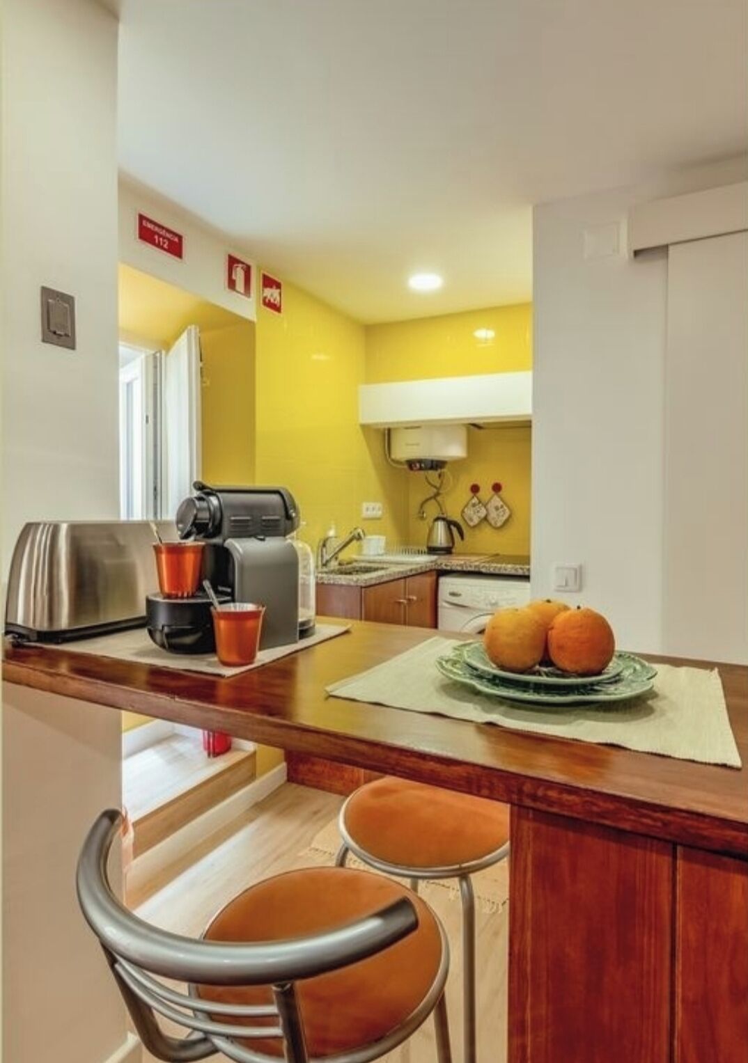 A compact kitchen with a coffee maker, toaster, and a fruit bowl on the counter.