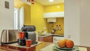 Une cuisine compacte équipée d’une machine à café, d’un grille-pain et d’un panier à fruits posé sur le plan de travail.
