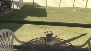 A patio with a round metal table and two white plastic chairs, a small potted plant, and a wooden fence in the background. - Jean's Cosy Sunny Cottage Sanctuary Point NSW Close to Palm Beach.
Netflix.  (Sanctuary Point)