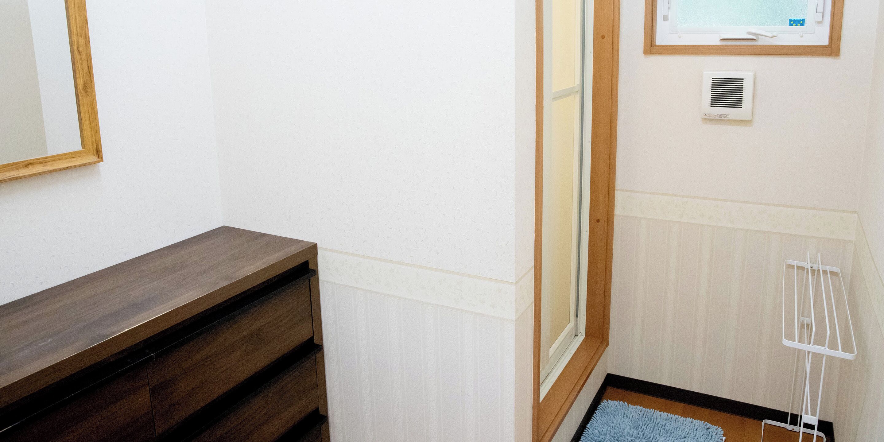 A corner of a room with a wooden bench, a radiator, a window, and a white wall.