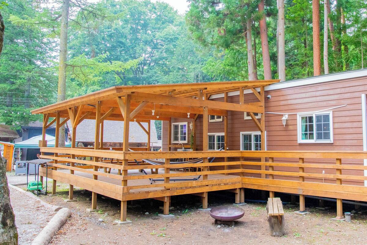 Eine Holzhütte mit Veranda und kleiner Terrasse, umgeben von Bäumen.