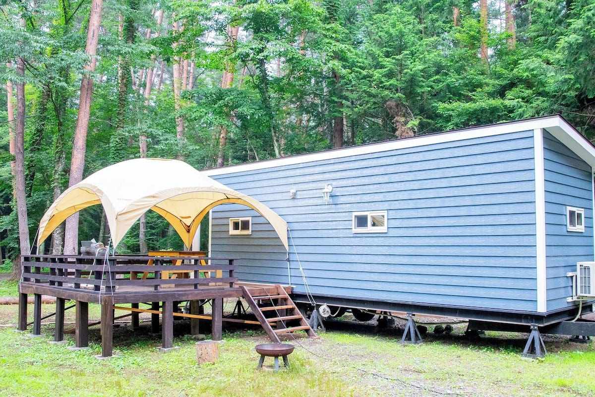 Ein blauer Wohnwagen mit überdachtem Außenbereich und einer Holzterrasse.