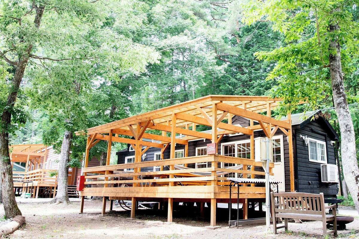 Eine Holzhütte mit einer Holzterrasse und einer Bank, umgeben von Bäumen.