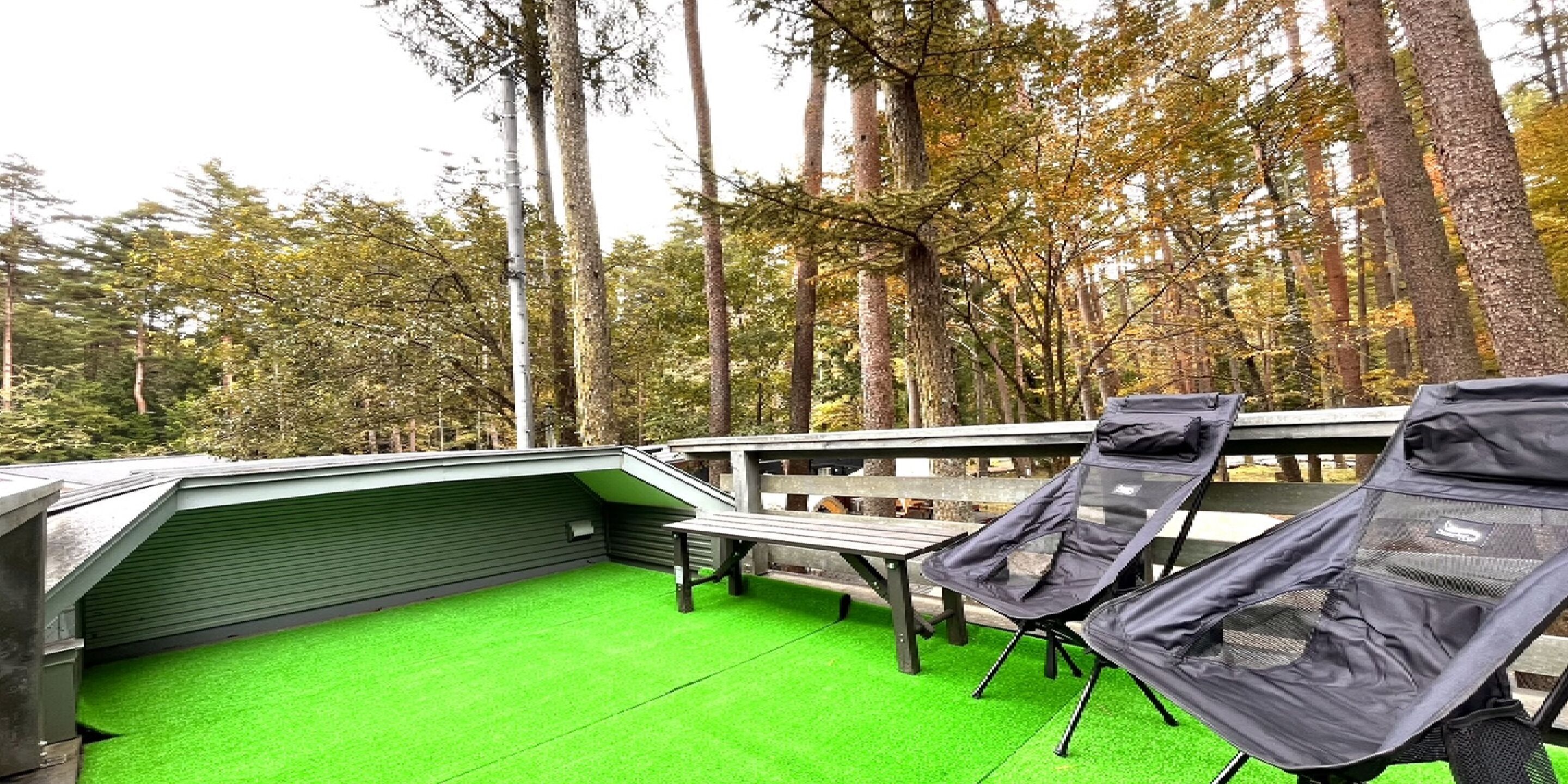 Un patio exterior con césped artificial verde, una parrilla y dos sillones de descanso.