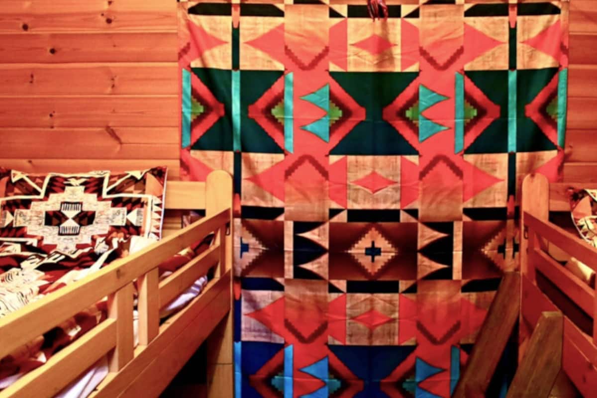 Ein Zimmer mit einem Doppelbett in der Mitte, zwei Einzelbetten an jeder Seite und einer Wand mit einem gemusterten Quilt.